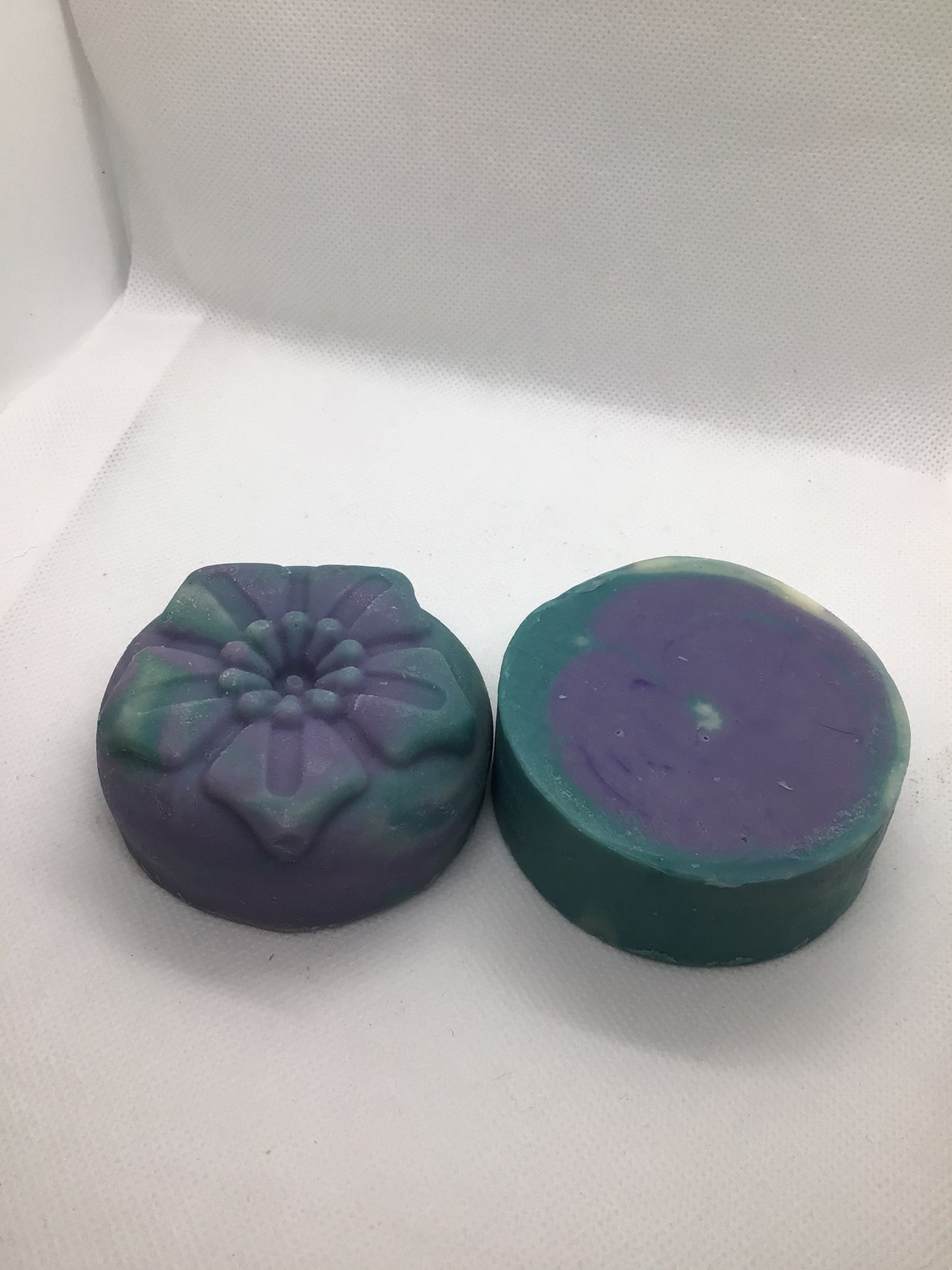 one round soap colored in blue purple and white, one flower shaped soap colored in blue and purple.